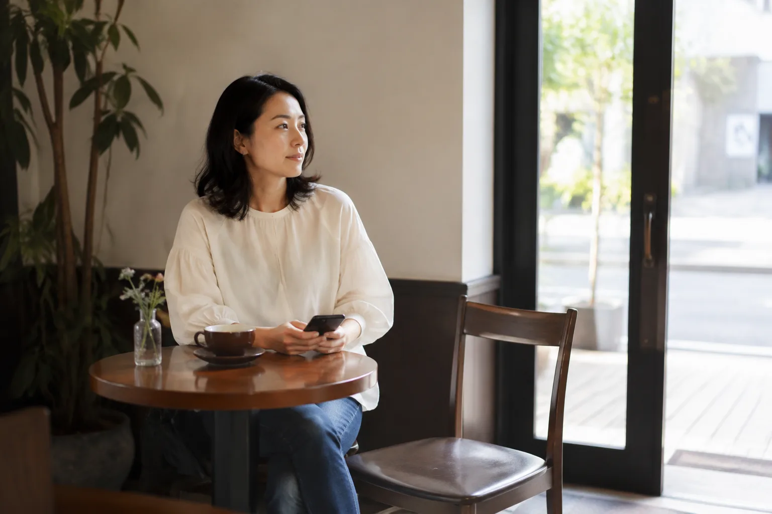 A woman holding her phone at a cafe table with an empty chair beside her